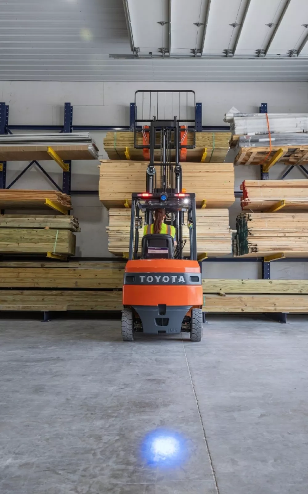 Toyota forklift moving lumber is a warehouse and using a pedestrian blue light and safety-enhanced parts.