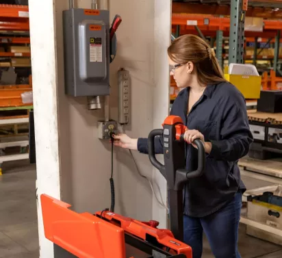Female associate plugging in battery on a Toyota electric pallet jack.