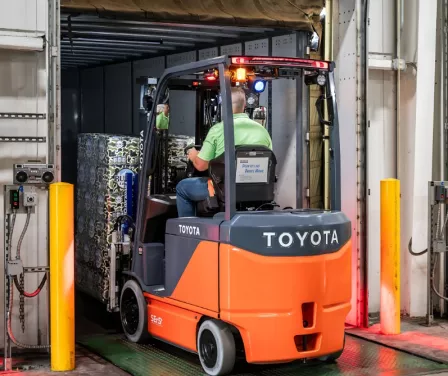 Toyota electric forklift driven by an operator backing out of a trailer and onto the dock floor.