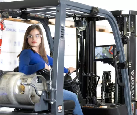 Toyota forklift operator driving in reverse to move product on the warehouse floor.