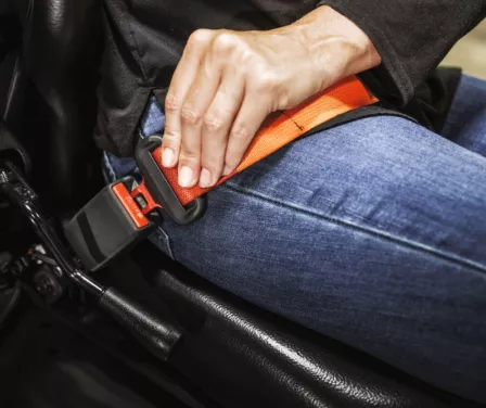 Forklift operator putting on a orange seatbelt while driving a Toyota forklift.