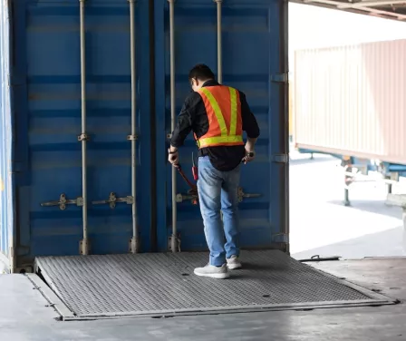 Warehouse worker on loading dock equipment preparing to unload semi-trailer.
