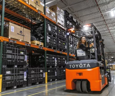 Toyota 3-wheel electric forklift with operator driving in warehouse.