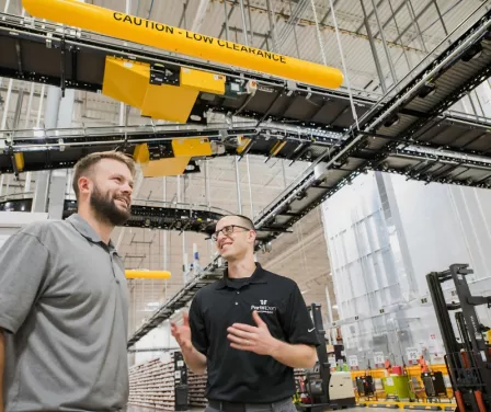 Warehouse associates speaking near automation equipment.