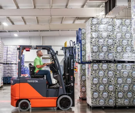 Operator on Toyota electric forklift lifting beverage products off the warehouse floor.