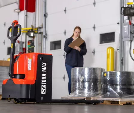 Warehouse worker checking product while using a Toyota ToraMax electric walkie pallet jack.