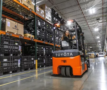 Forklift operator driving in reverse on a Toyota electric 3-wheel forklift in warehouse application.