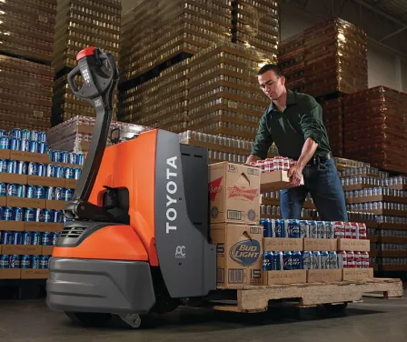 Forklift operator loading a Toyota electric pallet jack with beverage product.