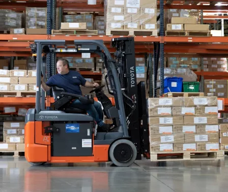 Toyota electric forklift driven backwards by forklift operator while carrying product.
