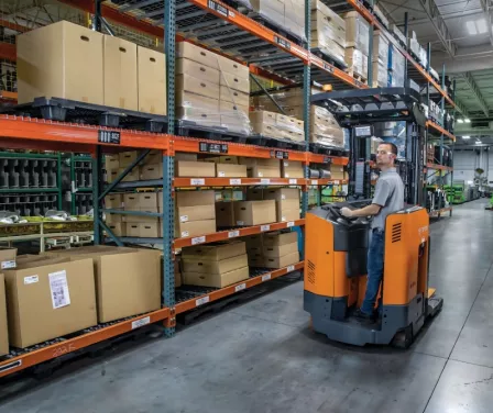 Toyota reach truck driven by operator near pallet racking.