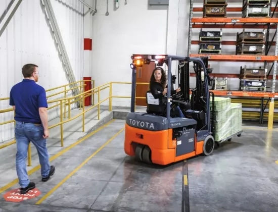 Toyota forklift operator driving near a pedestrian.