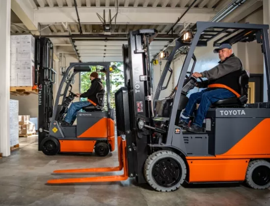 Two operators driving Toyota electric forklifts from the equipment fleet.