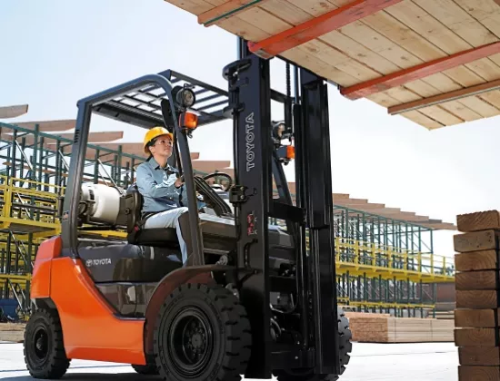 A forklift operator lifting lumber with a Toyota pneumatic tire forklift.