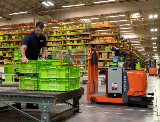 Warehouse associate unloading product from Toyota Core Tow Tractor automated guided vehicle.