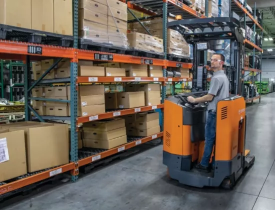 Operator driving a Toyota reach truck in a warehouse next to pallet racking.