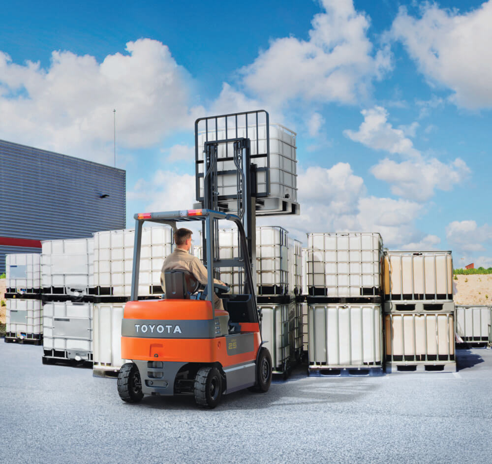 man using an orange and gray Toyota forklift to stack material outside