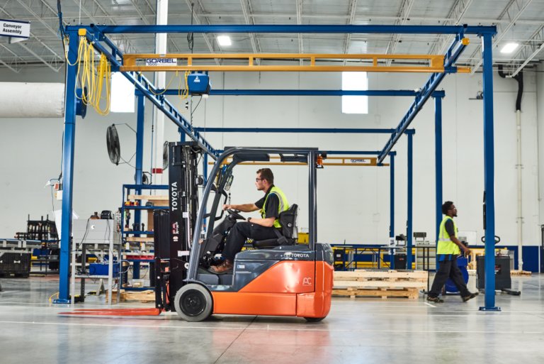a warehouse worker in a yellow safety vest and goggles is operating a Toyota forklift.